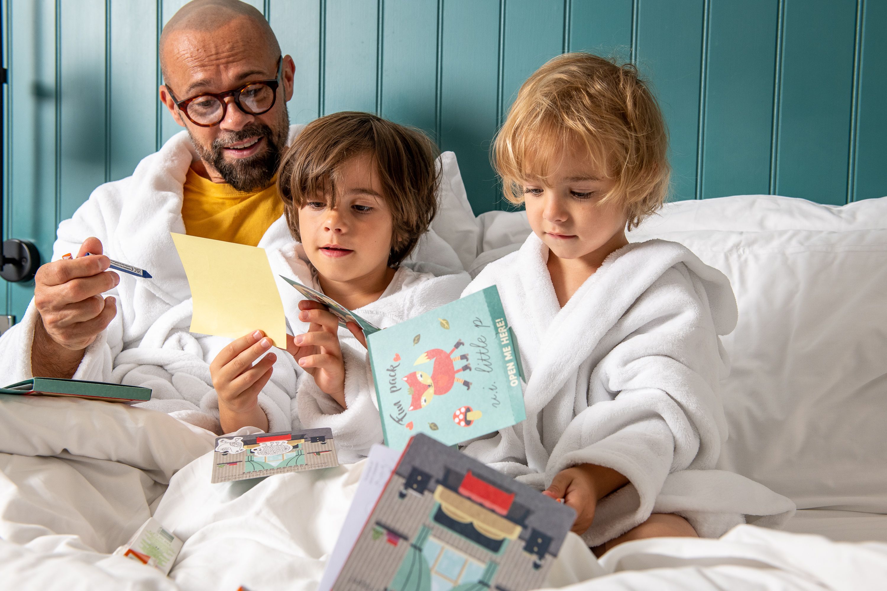 A dad colouring with his two sons in bed